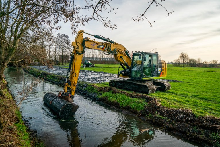 Met een machine wordt bagger uit de sloot op de kant geschept