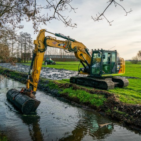 Met een machine wordt bagger uit de sloot op de kant geschept