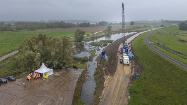 Drone foto van boven van zware machines op dijk en tent met mensen in oranje kleding er voor