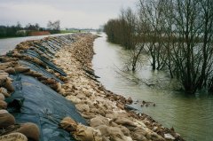Water staat hoog tegen een dijk die verstevigd is met zandzakken.