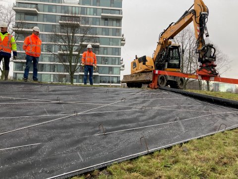 Medewerkers zetten de folie met krammen vast op de nieuwe dijk