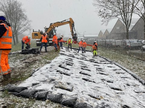 Medewerkers oefenen met het inpakken van de nieuwe dijk met folie