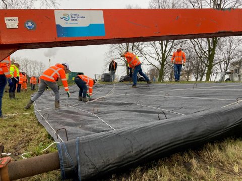 Medewerkers van het waterschap beschermen de nieuwe dijk met folie tegen hoogwater