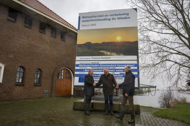 Bestuurders geven elkaar de hand voor het projectbord ter afronding van het project