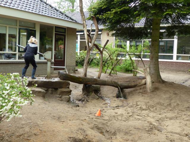Leerling bassischool Slingerbos speelt met waterpomp op schoolplein Slingerbos