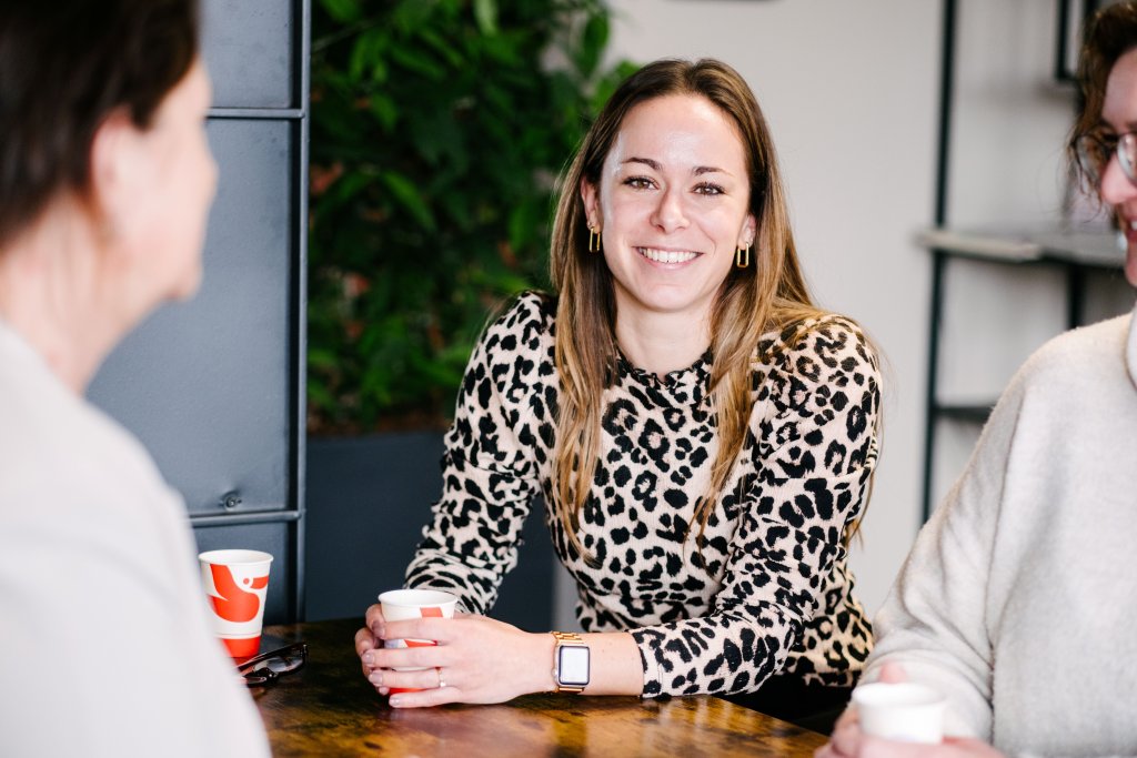 Glimlachende brunette met koffiekopje in haar hand, in overleg met twee andere dames.