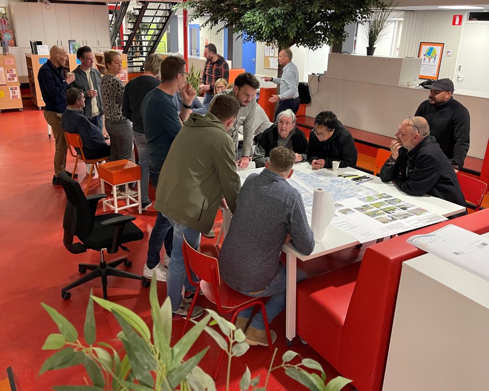 Bewoners en ontwerpers buigen zich samen over kaarten en plannen tijdens een drukbezochte klankbordgroepbijeenkomst
