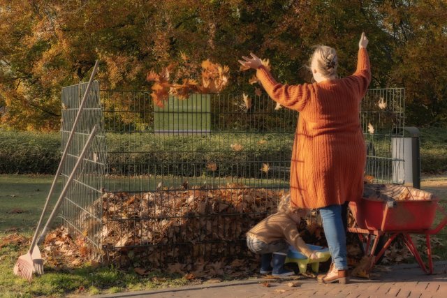 Moeder met kind storten bladeren in de bladkorf