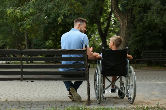 Vader met zoon in een rolstoel op een bankje in het bos