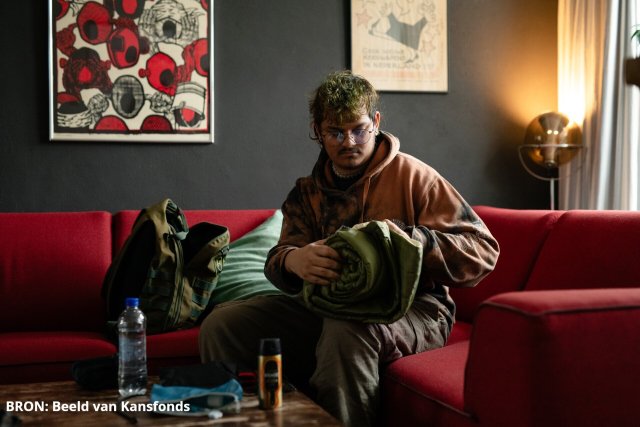 Jongen zittend op bank rolt slaapzak op