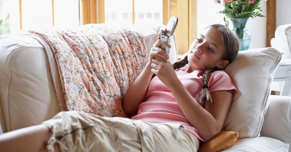 Puber met een mobiele telefoon ligt op een bank