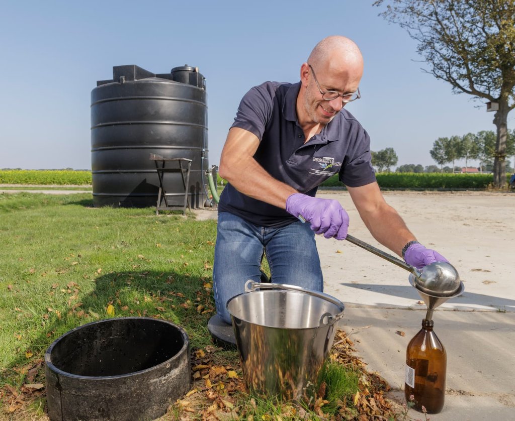 Medewerker Waterschap Zuiderzeeland giet middel in een fles op een erf bij een agrariër. 