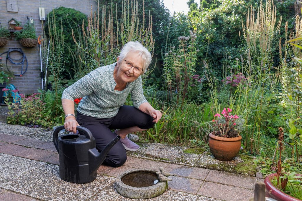 Marijke zit in haar tuin en houdt een gieter vast