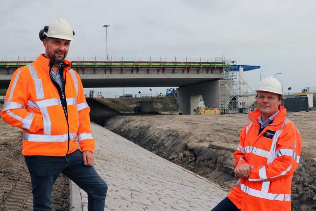 Benjamin en Bernd staan in veiligheidskleding buiten bij het laatste stukje Drontermeerdijk dat wordt versterkt.