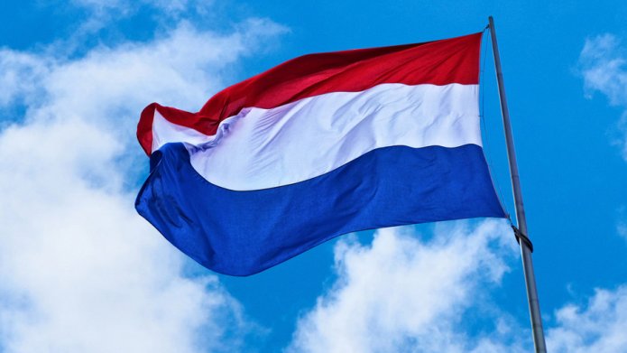Nederlandse vlag, rood, wit & blauw. Tegen blauwe hemel met witte wolken