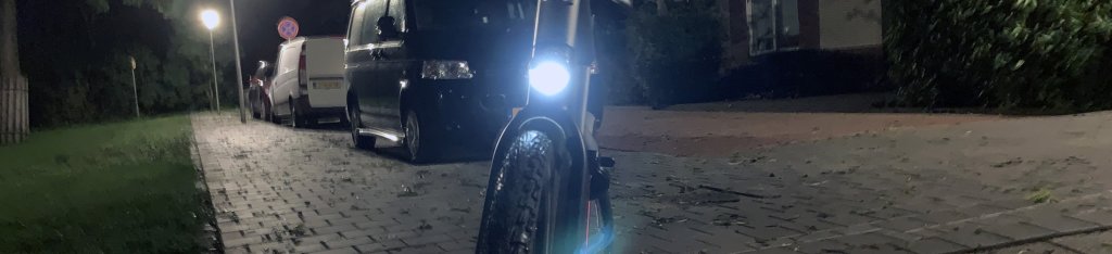Een fiets met voorlicht aan in het donker, op de grond is nog de reflectie van het rode achterlicht te zien
