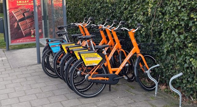 Oranje deelfietsen van Donkey Republic, geparkeerd in fietsenrek naast bushalte