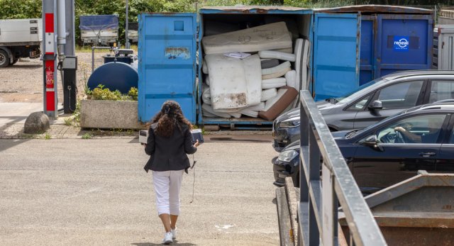 Vrouw loopt naar blauwe afvalcontainer